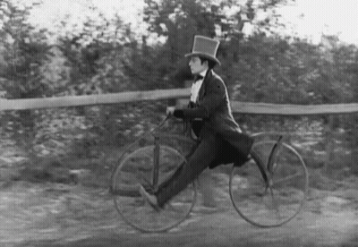 A Black And White Photo Of A Man In A Top Hat Riding A Bike . GIF