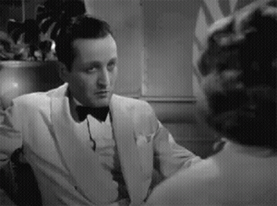 A Black And White Photo Of A Man In A Tuxedo Talking To A Woman . GIF