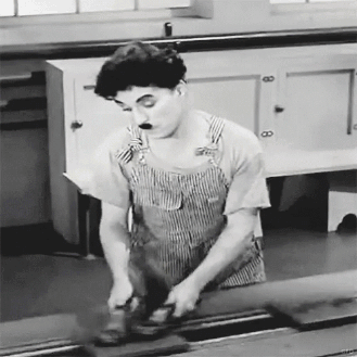 A Black And White Photo Of A Man In Overalls Using A Grinder . GIF