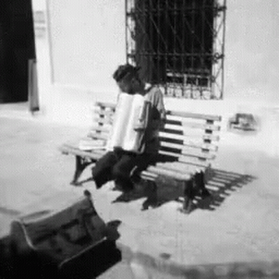 A Black And White Photo Of A Man Playing An Accordion On A Bench GIF