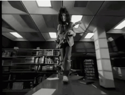 A Black And White Photo Of A Man Playing An Electric Guitar In A Library . GIF