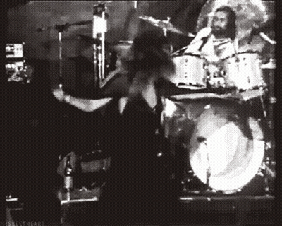 A Black And White Photo Of A Man Playing Drums In Front Of A Drum Set GIF