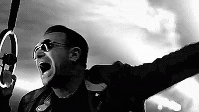 A Black And White Photo Of A Man Singing Into A Microphone While Holding A Ring . GIF