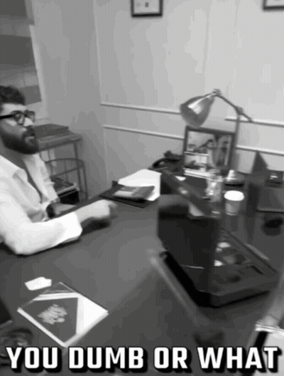A Black And White Photo Of A Man Sitting At A Desk With The Words You Dumb Or What Above Him GIF