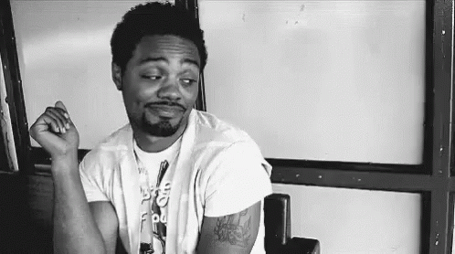 A Black And White Photo Of A Man Sitting In A Chair With His Hand On His Chin . GIF