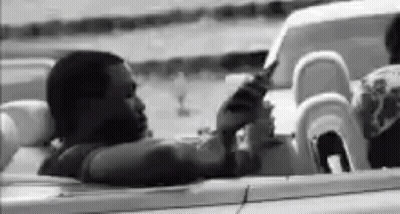 A Black And White Photo Of A Man Sitting In A Convertible . GIF