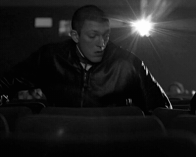 A Black And White Photo Of A Man Sitting In A Theater GIF