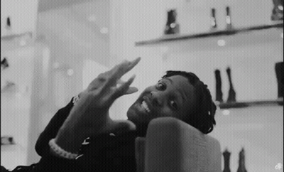 A Black And White Photo Of A Man Sitting On A Couch With His Hands Up . GIF