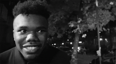 A Black And White Photo Of A Man Smiling With A Car In The Background GIF