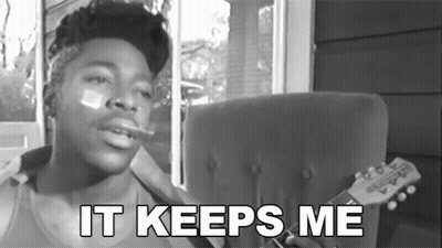 A Black And White Photo Of A Man Smoking A Cigarette With The Words " It Keeps Me " Below Him GIF