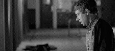 A Black And White Photo Of A Man Standing In A Hallway Looking Down . GIF