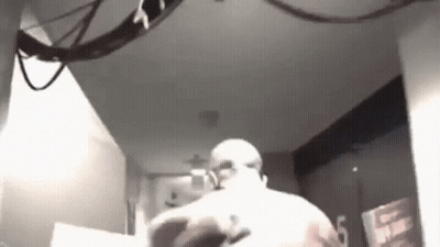 A Black And White Photo Of A Man Standing In A Room With A Ceiling Fan . GIF