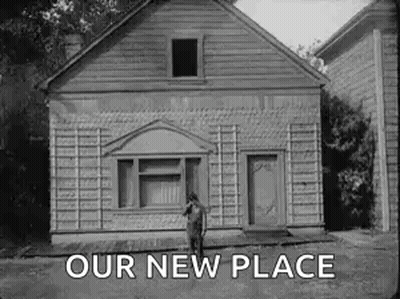 A Black And White Photo Of A Man Standing In Front Of A House With The Words `` Our New Place '' Above Him . GIF
