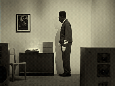 A Black And White Photo Of A Man Standing In Front Of A Record Player With A Box That Says B&w National On It GIF