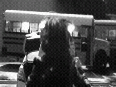 A Black And White Photo Of A Man Standing In Front Of A School Bus GIF