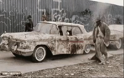 A Black And White Photo Of A Man Standing Next To A Dirty Old Car . GIF