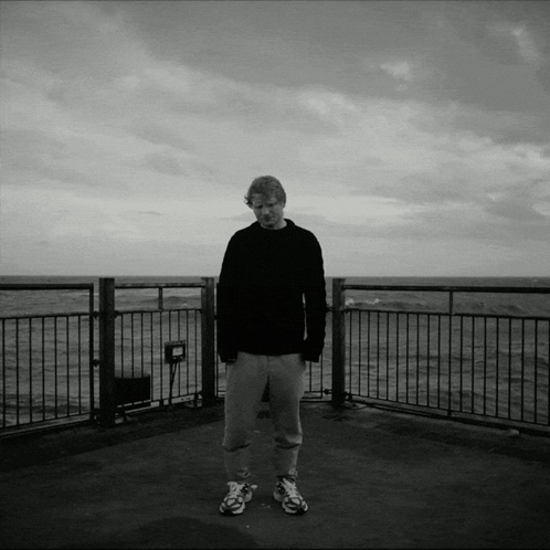 A Black And White Photo Of A Man Standing On A Balcony Overlooking A Body Of Water GIF