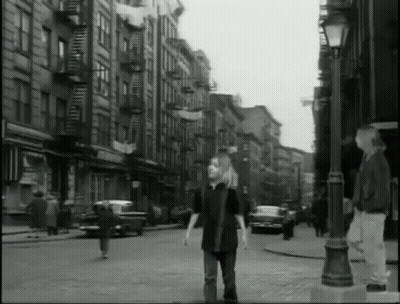 A Black And White Photo Of A Man Walking Down A City Street GIF