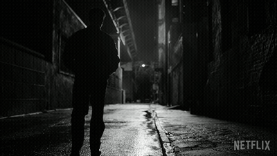 A Black And White Photo Of A Man Walking Down A Dark Alleyway With Netflix Written In The Corner GIF