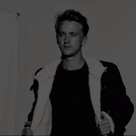 A Black And White Photo Of A Man Wearing A Black Jacket With A White Fur Collar GIF