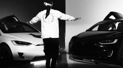 A Black And White Photo Of A Man Wearing A Christian Dior Shirt Standing Next To Two Cars GIF