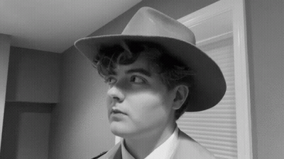 A Black And White Photo Of A Man Wearing A Hat And A Suit GIF