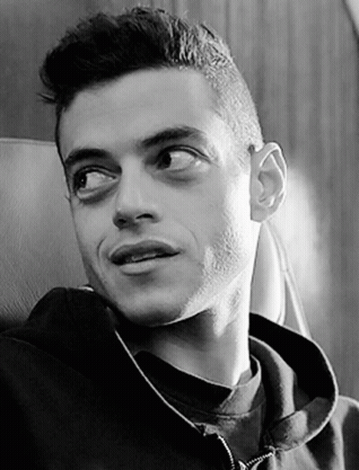 A Black And White Photo Of A Man Wearing A Hoodie Sitting In A Chair . GIF