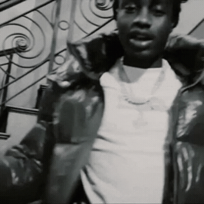 A Black And White Photo Of A Man Wearing A Jacket And A Necklace . GIF