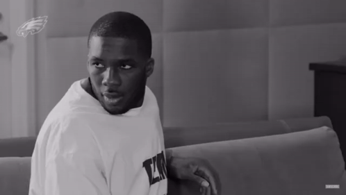 A Black And White Photo Of A Man Wearing A White Shirt With The Letter L On It GIF