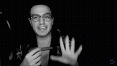 A Black And White Photo Of A Man Wearing Glasses Holding Something In His Hand . GIF