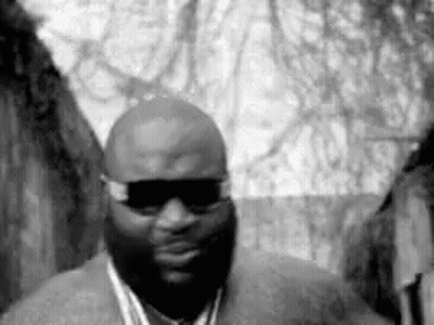A Black And White Photo Of A Man Wearing Sunglasses And A Chain Around His Neck . GIF