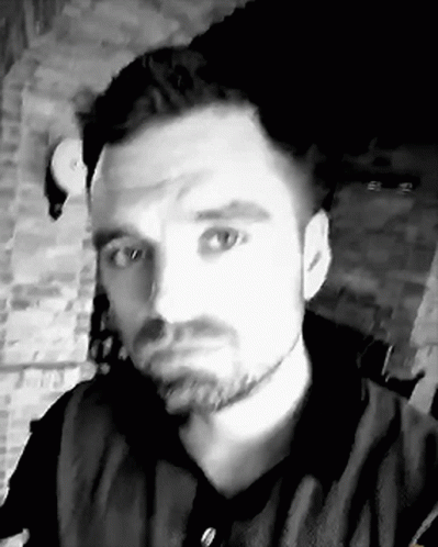 A Black And White Photo Of A Man With A Beard Taking A Selfie In Front Of A Brick Wall . GIF