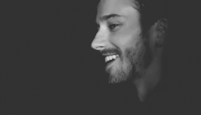 A Black And White Photo Of A Man With A Beard Wearing A Hat And Smiling . GIF