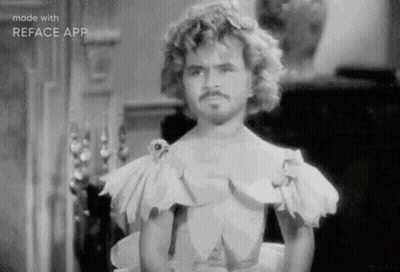 A Black And White Photo Of A Man With Curly Hair And A Mustache Wearing A Dress . GIF