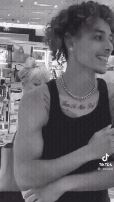 A Black And White Photo Of A Man With Curly Hair And A Tattoo On His Chest GIF