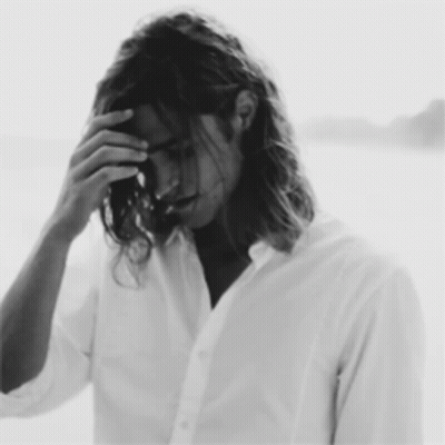 A Black And White Photo Of A Man With Long Hair Covering His Face GIF