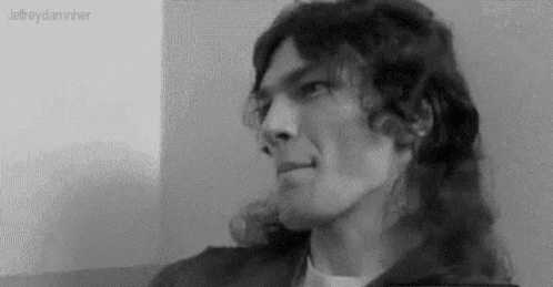 A Black And White Photo Of A Man With Long Hair Looking At The Camera . GIF