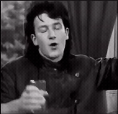A Black And White Photo Of A Man With Long Hair Singing Into A Microphone GIF