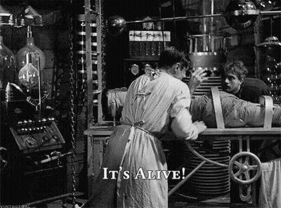 A Black And White Photo Of A Man Working On A Mummy With The Words It 'S Alive Below Him GIF