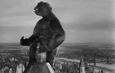 A Black And White Photo Of A Monster Standing On Top Of A Building In Front Of A City . GIF