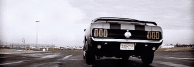 A Black And White Photo Of A Mustang Driving Down A Road . GIF