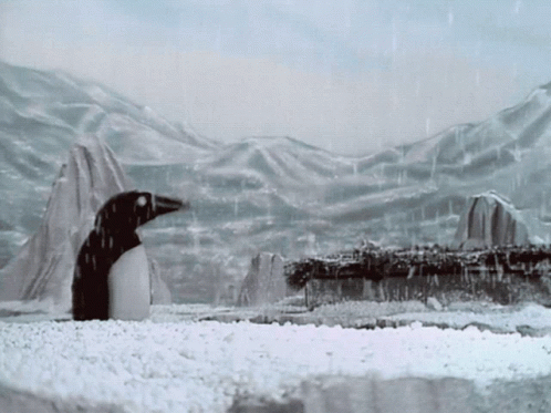 A Black And White Photo Of A Penguin In The Snow With Mountains In The Background GIF