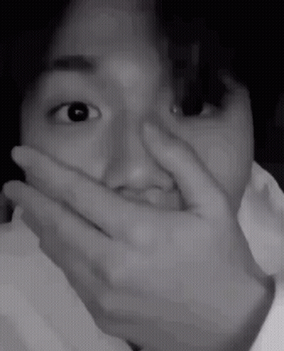 A Black And White Photo Of A Person Covering Their Mouth With Their Hand . GIF