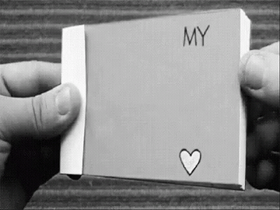 A Black And White Photo Of A Person Holding A Piece Of Paper With The Word `` My '' And A Heart Drawn On It . GIF