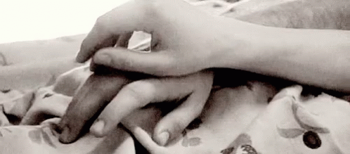 A Black And White Photo Of A Person Holding Another Person 'S Hand On A Bed . GIF