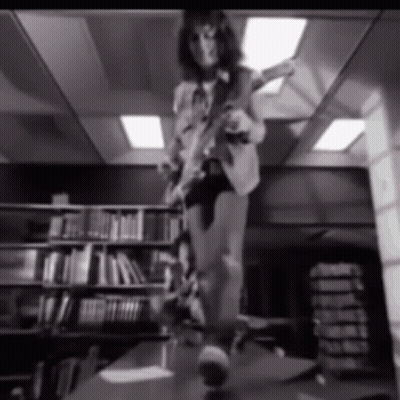 A Black And White Photo Of A Person Playing A Guitar In A Library GIF