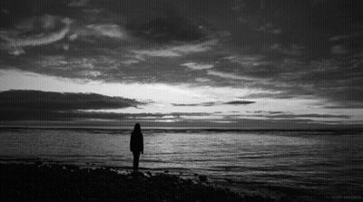 A Black And White Photo Of A Person Standing In Front Of A Body Of Water GIF
