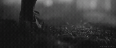 A Black And White Photo Of A Person Standing In The Grass With A Gun . GIF