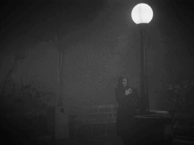 A Black And White Photo Of A Person Standing Under A Street Light . GIF