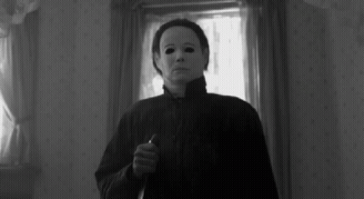 A Black And White Photo Of A Person Wearing A Mask Holding A Knife In A Room . GIF